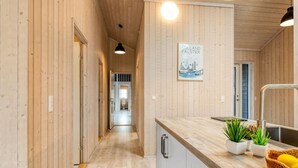 A narrow hallway with wooden walls and a wooden ceiling, leading to a bathroom.