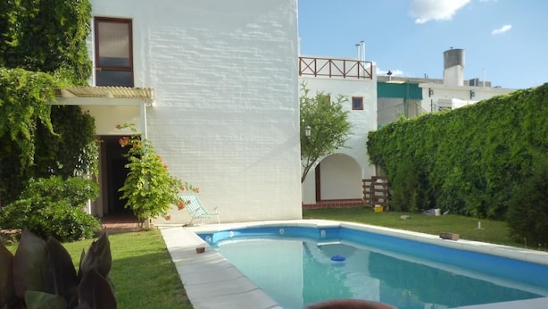A swimming pool with a white house in the background, surrounded by greenery and a clear sky. - Casa de Piedra (Mina Clavero)