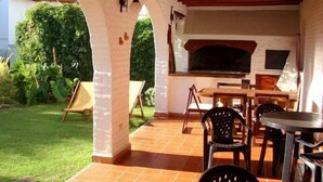 An outdoor patio with a brick floor, a table, chairs, and a grill. - Casa de Piedra (Mina Clavero)