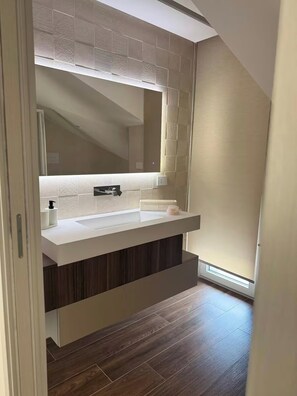 Een moderne badkamer met een grote spiegel, een wit wastafelmeubel en vloerbedekking van donker hout.