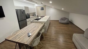 Une cuisine moderne équipée d’un four encastré, d’un évier et d’une cuisinière. On y trouve une table à manger avec des chaises, ainsi qu’un fauteuil en forme de poire dans l’espace salon.