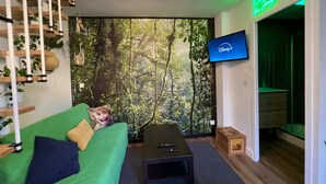 A modern living room with a green sofa, a small table, a TV on the wall, and a forest mural. - Quiet & Stylish Home With Garden (Le Mans)