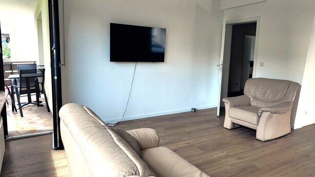 A living room with a beige sofa, a leather armchair, and a flat-screen TV mounted on the wall. - Apartment in Adenau (Adenau)