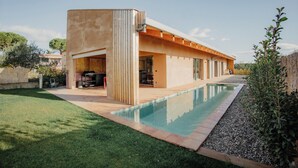 Una casa moderna con piscina, un porche cubierto y un césped bien cuidado.