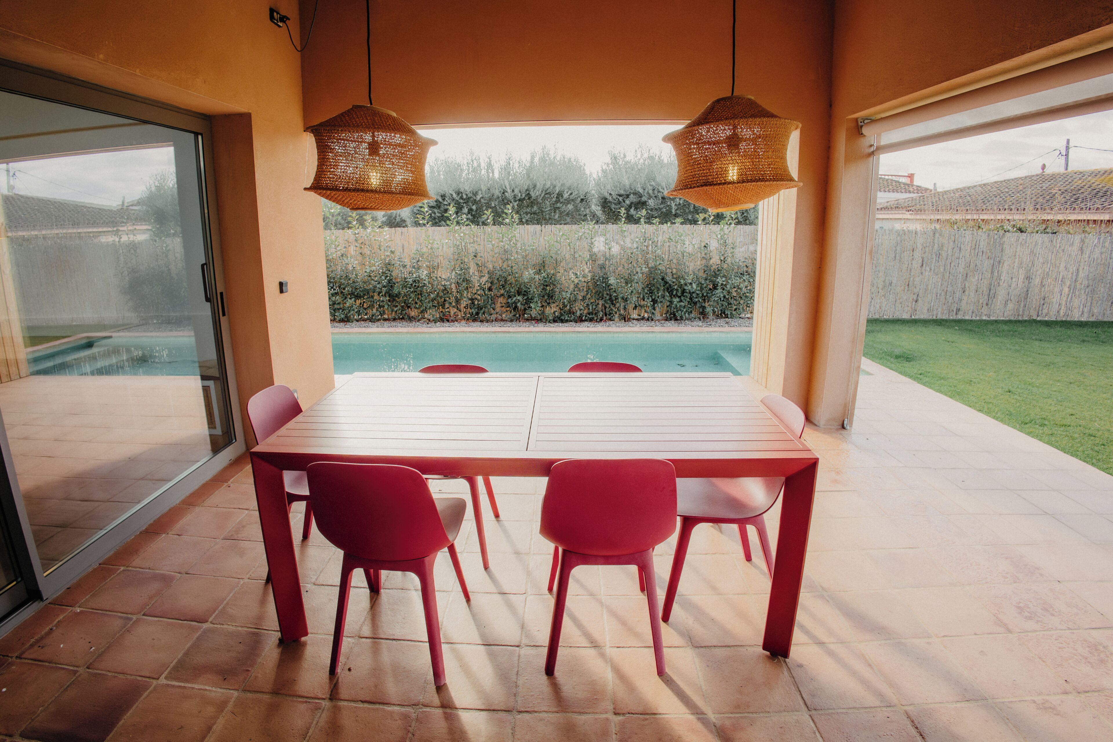 A dining area with a table and chairs, a view of a swimming pool, and a covered patio.