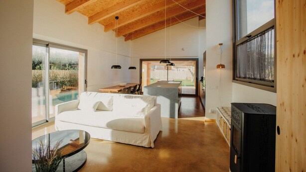 Un salón amplio con un sofá blanco, una mesa de centro de cristal y techo de madera.