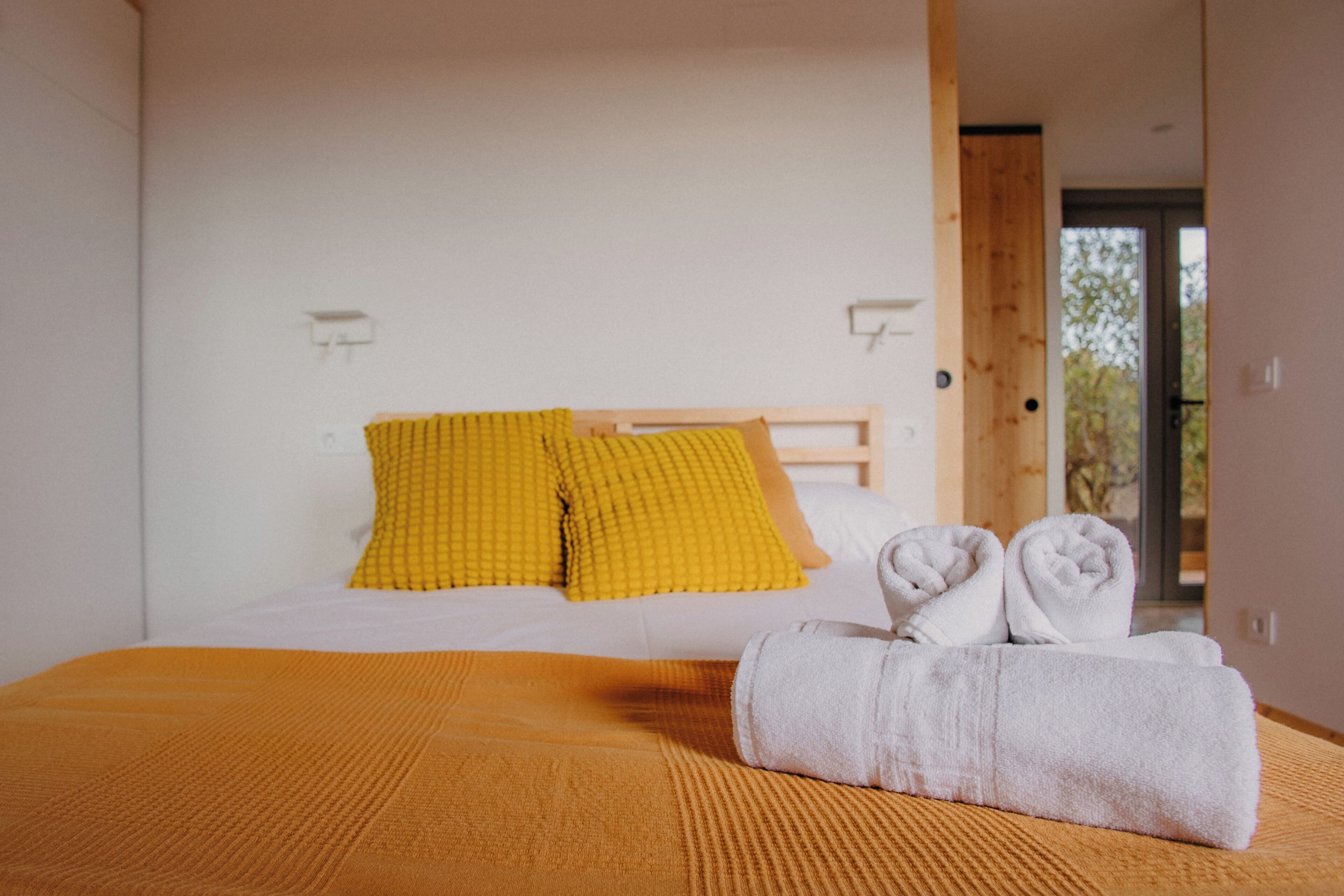 A bedroom with a bed, two pillows, a blanket, and two towels.