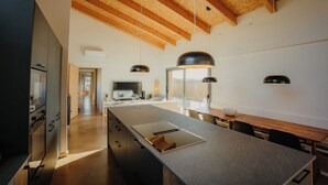 Una cocina moderna con vigas de madera, una isla grande, luces colgantes y vistas al exterior.