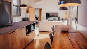 A modern kitchen with wooden cabinets, a dining table, and pendant lighting. - Empordà Soul, modern country house with pool (Sant Miquel de Fluvià)