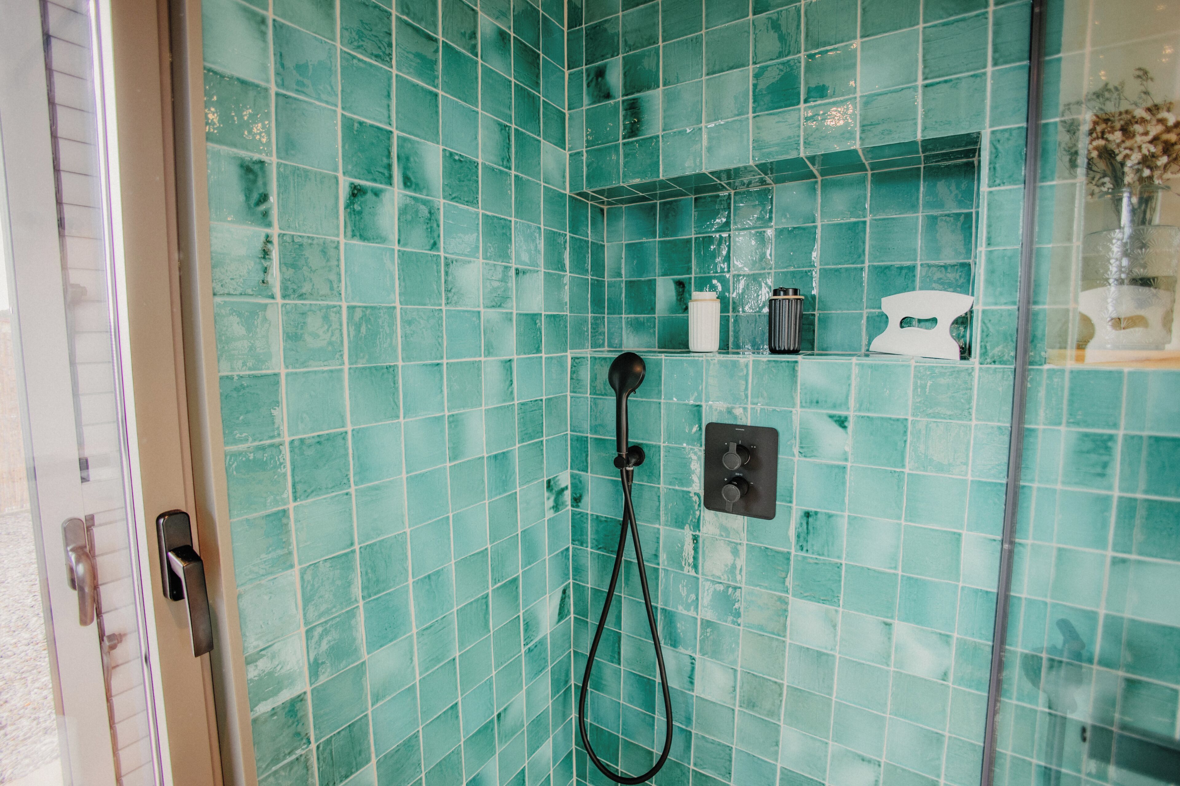 Ein Badezimmer mit türkisblauen Fliesen, einer Duschbrause und einer kleinen Ablage mit Pflegeprodukten.