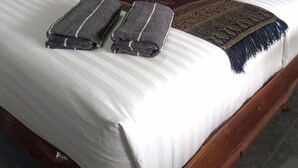 A neatly made bed with a patterned bedspread, two folded towels, and two bright pink pillows. - MG Guest House (Thani)