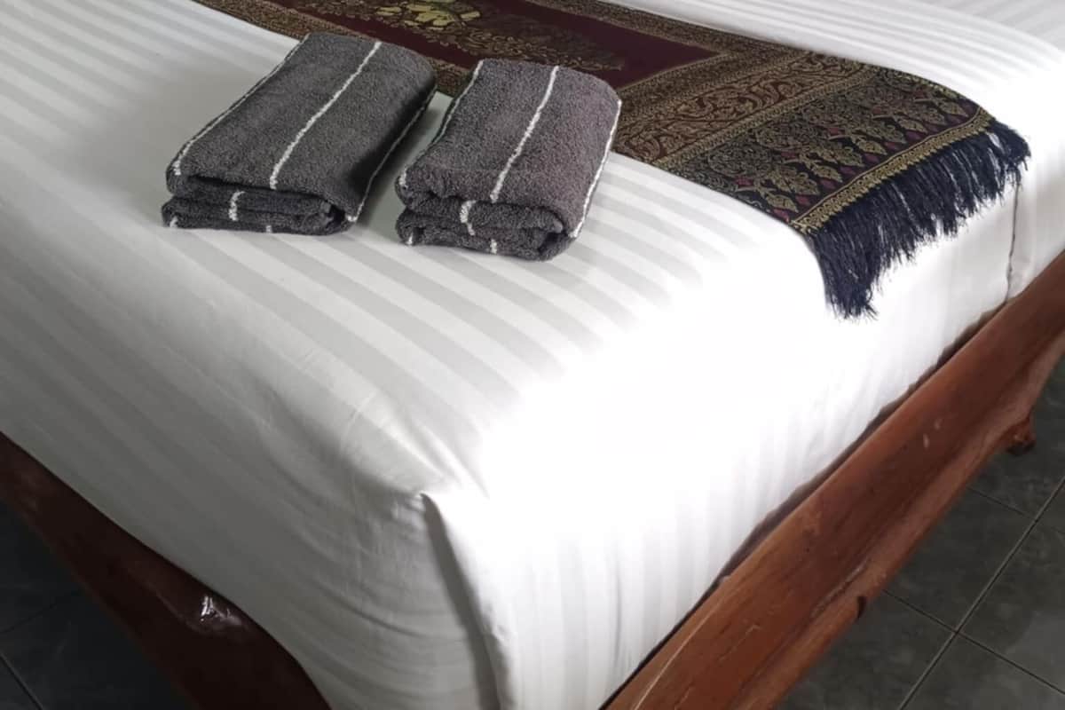 A neatly made bed with a patterned bedspread, two folded towels, and two bright pink pillows.