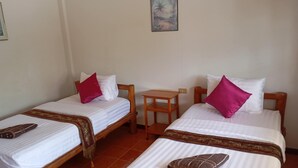 A room with two single beds, each with a wooden frame, white bedding, and a red pillow. There is a small wooden table between the beds, and a framed picture on the wall above the beds. - MG Guest House (Thani)