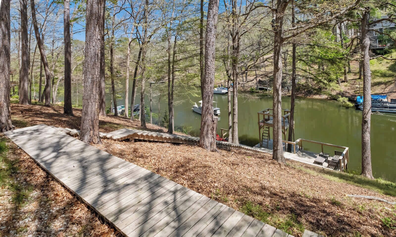 A wooden deck overlooking a calm lake with boats, surrounded by trees.