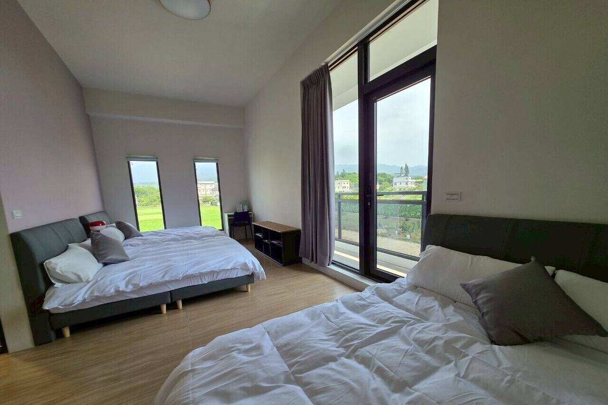 Una habitación de hotel moderna con dos camas, un escritorio pequeño y ventanas amplias con vistas al exterior.