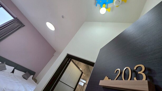 Une chambre d’hôtel avec un lit, un ventilateur de plafond et un panneau indiquant le numéro de la chambre, fixé au mur.