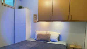 A bedroom with a bed, a nightstand, a wardrobe, and a small shelf with a plant. - Apartment in Nieuwpoort Near the Beach (Nieuwpoort)