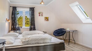 A bedroom with a bed, a desk, a chair, a skylight, and a window with curtains.