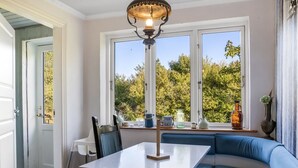 A dining area with a table and chairs, a blue cushioned bench, a window with a view of trees, and a pendant light.