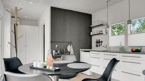 A modern kitchen with white cabinets, a black dining table, and two black chairs. There is a window with a view of trees, and a black wall with vertical lines. - "Konrad" - 300m from the sea by Interhome (Hals)