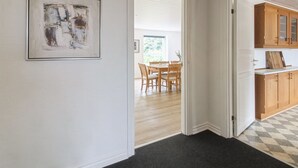 A hallway with a framed abstract painting, a dining area with wooden chairs and a table, and a kitchen with wooden cabinets.