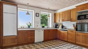 A kitchen with wooden cabinets, a white refrigerator, a dishwasher, a checkered floor, a window with a view, and a clock on the wall.