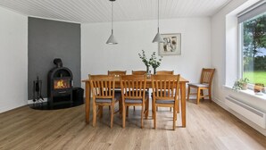 A dining area with a wooden table and chairs, a fireplace, and a window with a view of greenery.