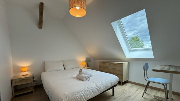 A bedroom with a bed, bedside lamps, a desk, a chair, a window, and a ceiling light fixture. - Cottage in Saint-vincent Near Le Mans (Saint-Vincent-du-Lorouër)