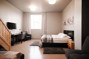 A bedroom with a bed, desk, chair, TV, and artwork on the wall. - hotel Grindavik (Grindavik)