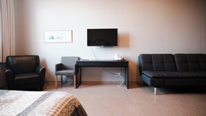Quarto de hotel com cama, escrivaninha, televisão, sofá e poltrona.
