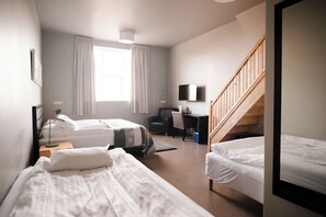 A hotel room with two beds, a desk, a chair, a TV, and a staircase. - hotel Grindavik (Grindavik)