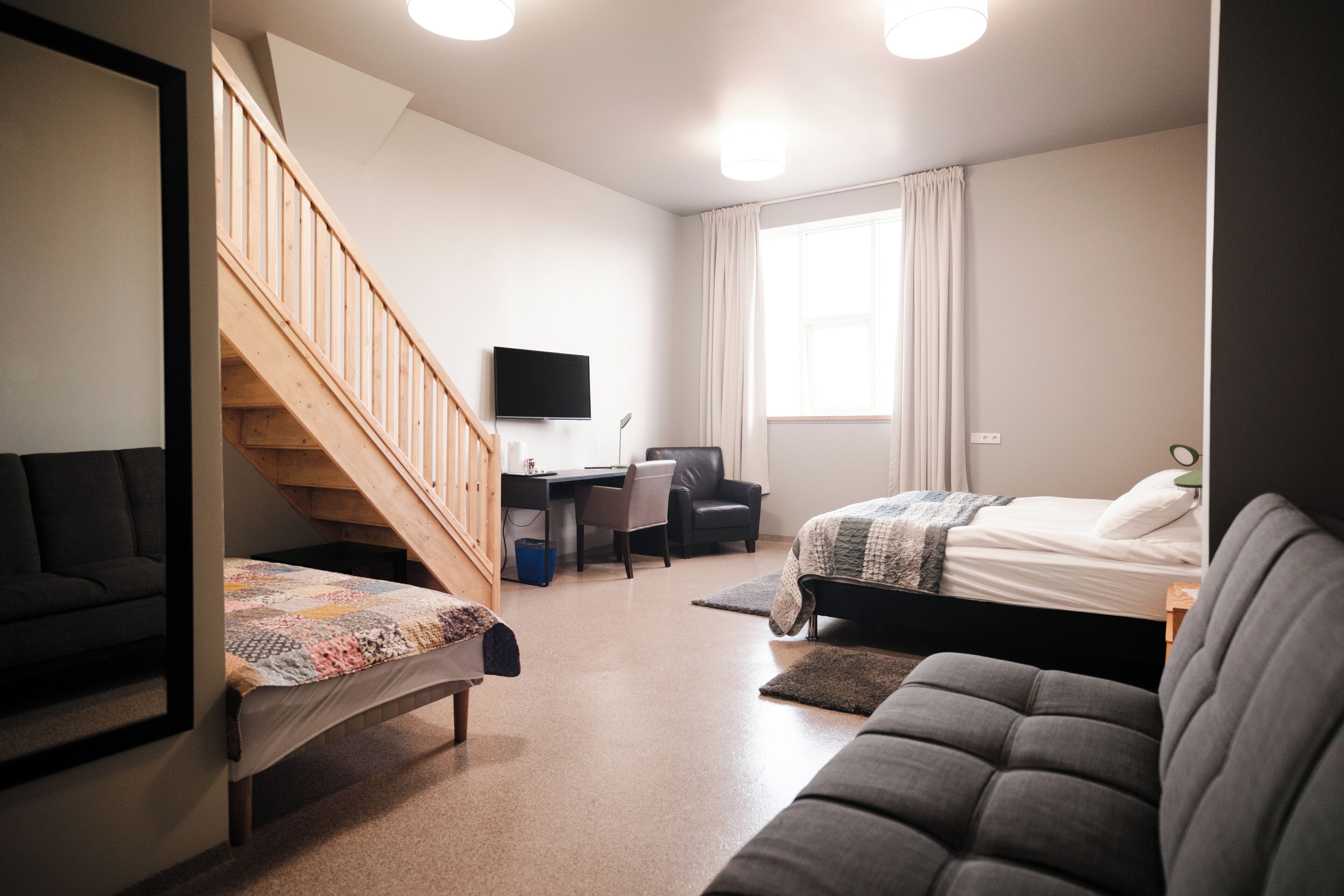 Une pièce moderne et bien éclairée, avec un escalier en bois, un bureau, un lit et un canapé.