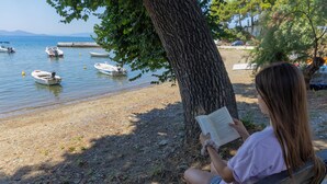Eine Person sitzt an einer Bank an einem See, im Wasser sind Boote.