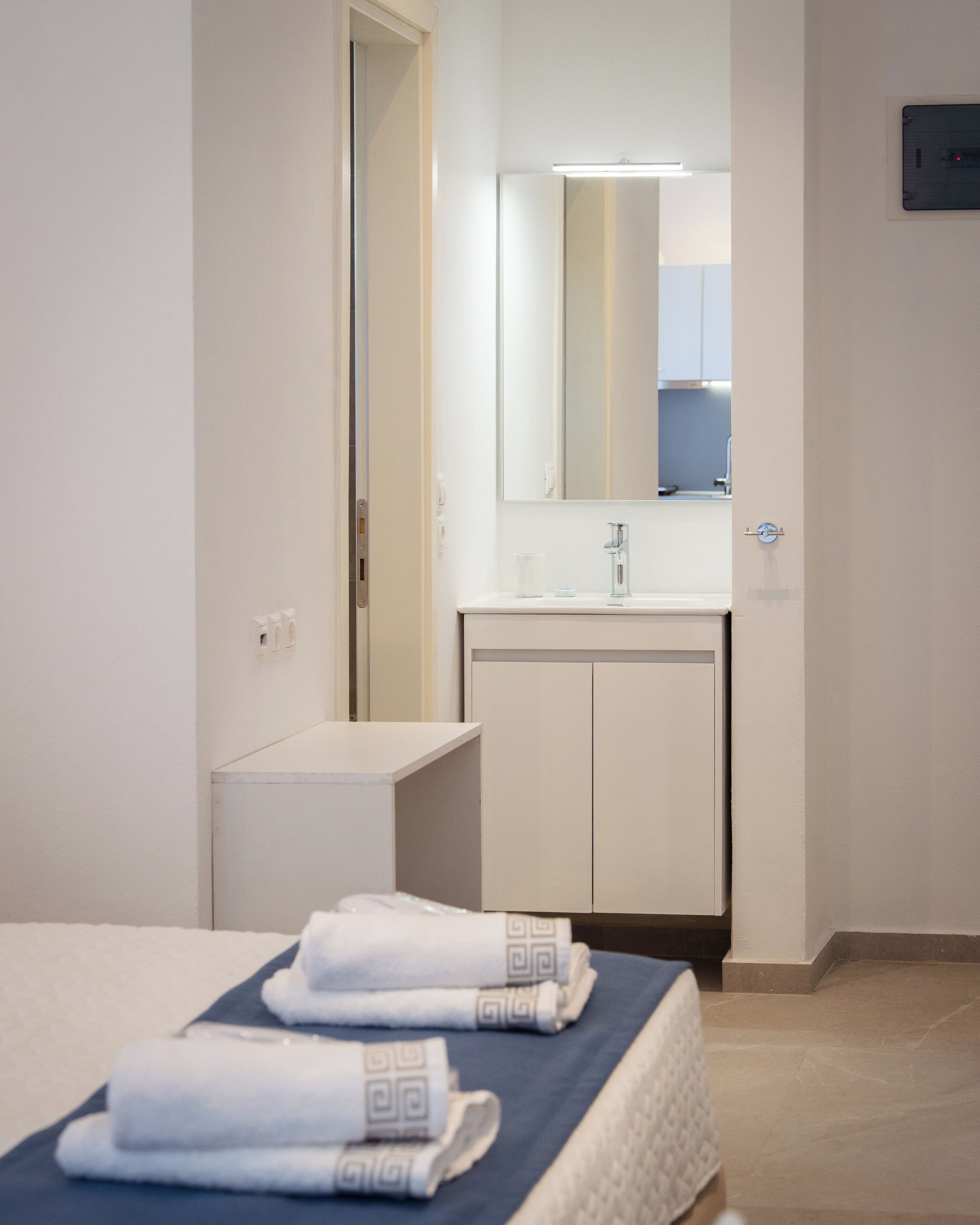 Una habitación de hotel con cama, mesita de noche, espejo, lavabo y toalla.