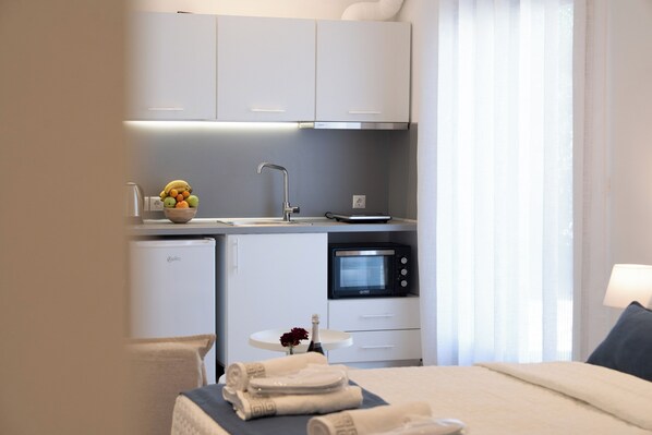 A compact kitchenette with a refrigerator, microwave, and a bowl of fruit. There is a small table with a flower vase and towels. - Afissos Blu Hotel (South Pelion)