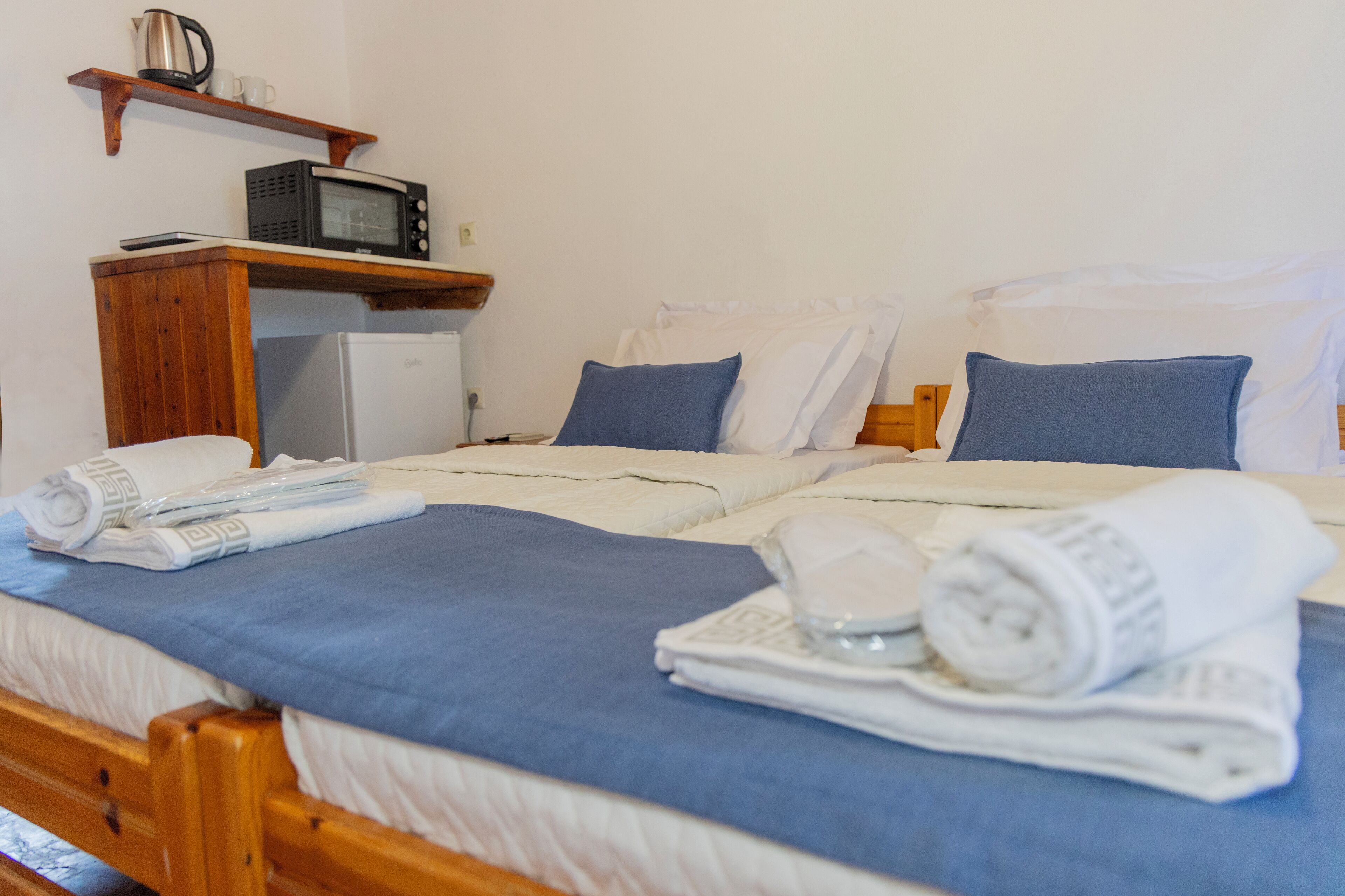 Une chambre d’hôtel équipée d’un lit, d’un petit réfrigérateur, d’un four à micro-ondes et d’une étagère avec une bouilloire et des tasses.