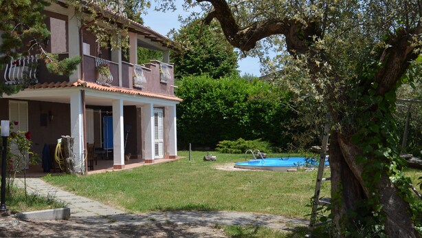 A two-story house with a balcony, a swimming pool, and a large tree in the yard.