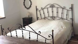 A room with a bed, a wooden table, a nightstand, a mirror, and a chandelier.