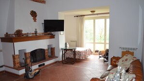 A living room with a fireplace, a television, a sofa, and a table with a floral tablecloth.