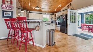 A kitchen with wooden ceiling, red bar stools, and a stainless steel trash can.