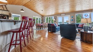 A spacious living area with a wooden ceiling, a kitchen bar with red barstools, and a sofa.