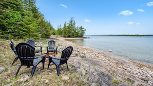 A lakeside setting with a table and chairs by the water, surrounded by trees.