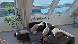 A modern loft apartment with a large gray sectional sofa, a small table, and a potted plant. There are skylights providing natural light and a view of the cityscape. - Villa near Annecy with swimming pool (Fillière)