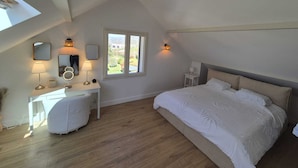A bedroom with a sloped ceiling, a bed with a headboard, a vanity with a mirror, and a window with a view of greenery. - Villa near Annecy with swimming pool (Fillière)