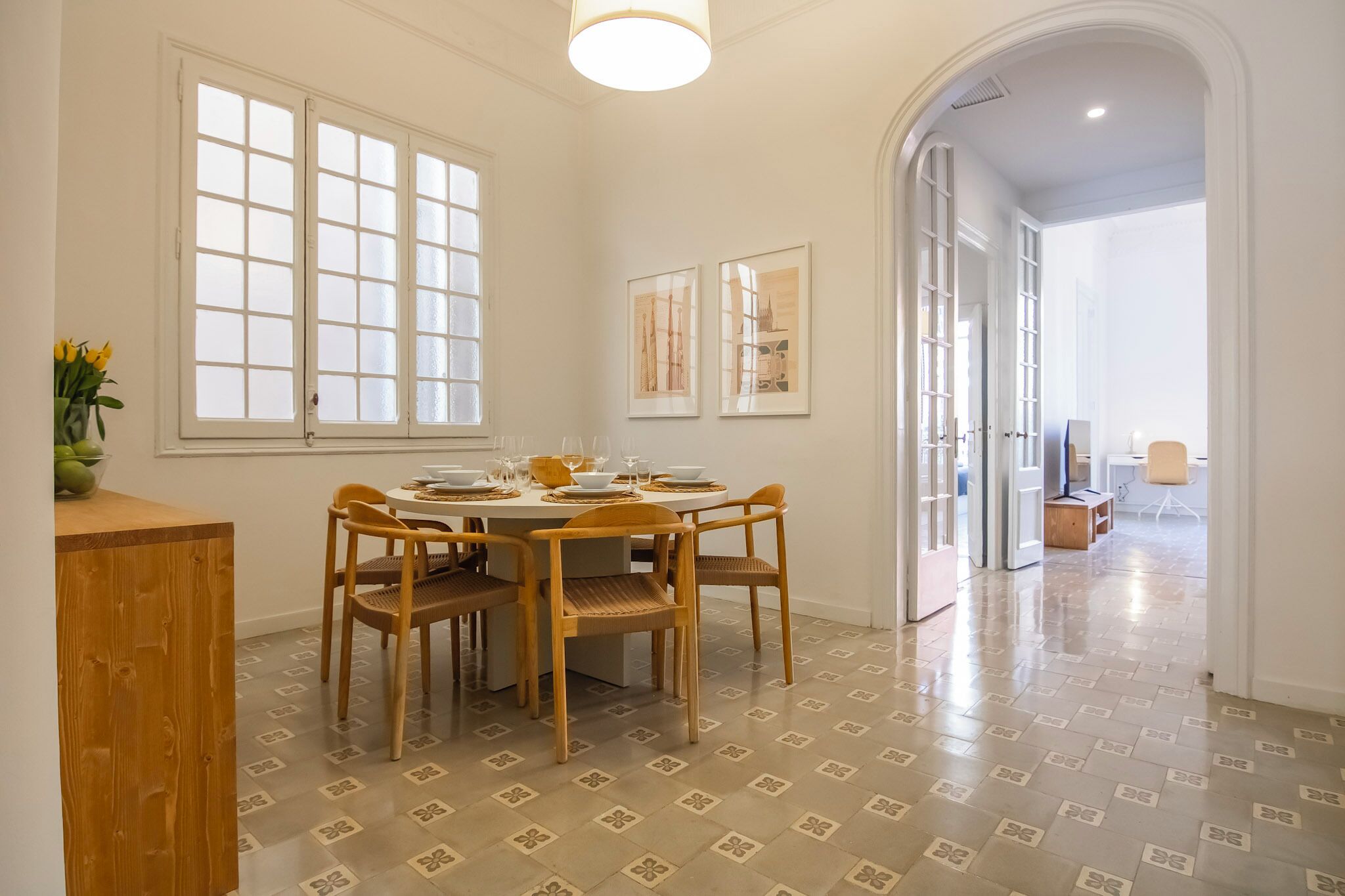 A dining area with a round table and six chairs, a window with frosted glass, and a patterned floor.