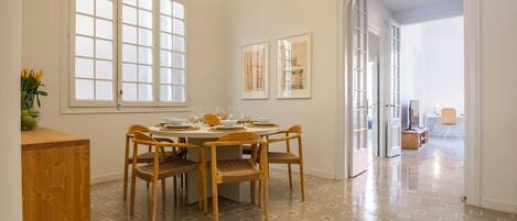 A dining area with a round table and six chairs, a window with frosted glass, and a patterned floor.