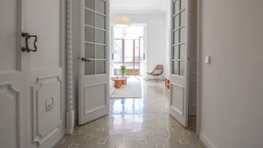 Un pasillo con puertas blancas que dan a una sala de estar con un sofá, una silla y una mesa.