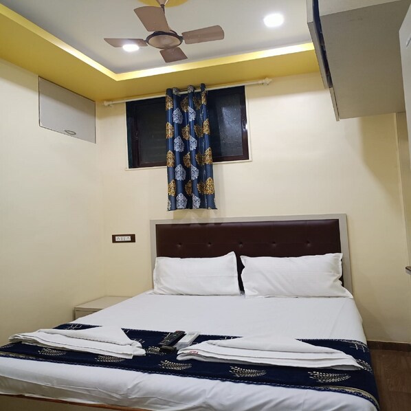 A bedroom with a bed, a ceiling fan, a window with curtains, and a wall socket.