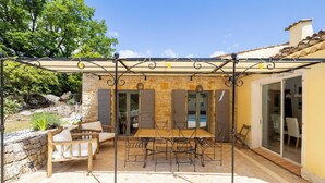 Eine Terrasse im Freien mit einem Steintisch und Stühlen, einer Pergola und einer Steinmauer.