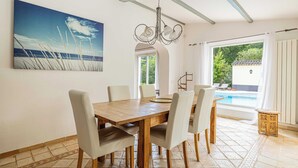 Ein Essbereich mit einem Holztisch und Stühlen, einer Kristallleuchtre und einem großen Gemälde mit Strandmotiv an der Wand.